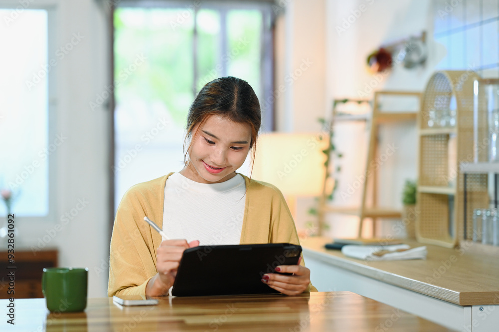Young woman in casual clothes using digital tablet sitting in a modern kitchen Young woman in casual clothes using digital tablet sitting in a modern kitchen