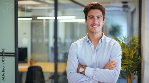 Smiling handsome businessman with crossed arms in modern office,young man exuding confidence, business success concept.