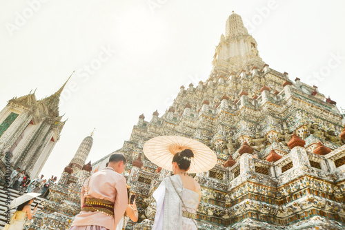 Bangkok, Thailand - 11th february, 2024: young thai couple wear traditional clothes for photo session by Wat Arun beautiful buddhist temple on hot sunny day photo