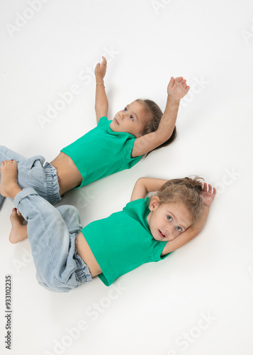 Two little girls in green t-shirts and jeans are sitting down, having fun. photo