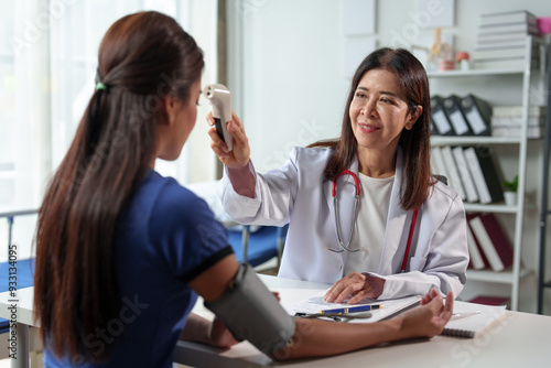 Asian female doctor uses infrared forehead thermometer to check woman's body temperature before vaccination at clinic or hospital. treatment concept health care.