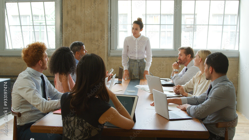 © Monkey Business - Young Businesswoman Giving Presentation To Multi-Cultural Team Sitting Around Table In Modern Office