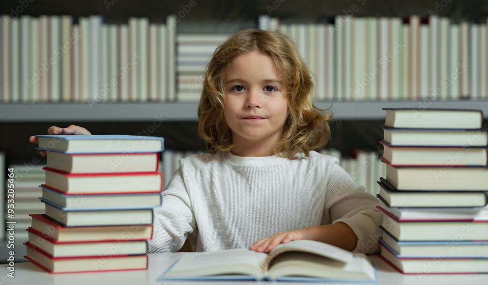 Knowledge day. School boy doing homework on desk in school library. Pupil child studying homework literature near pile of books. Kid reads a book with shelves stacks of books in the background. Knowledge day. School boy doing homework on desk in school library. Pupil child studying homework literature near pile of books. Kid reads a book with shelves stacks of books in the background.