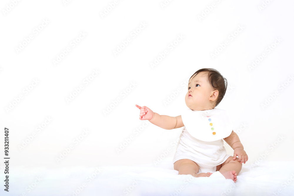 白背景の前に座り笑顔で指差しする女の子の赤ちゃん。お勧めポーズ,コピースペースあり 白背景の前に座り笑顔で指差しする女の子の赤ちゃん。お勧めポーズ,コピースペースあり