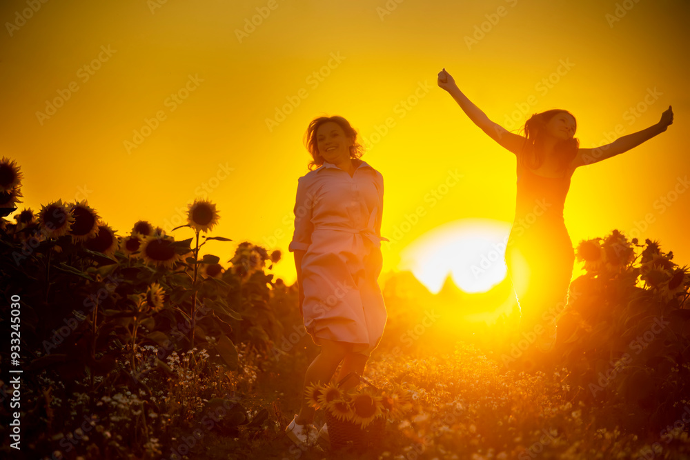 Fototapeta premium A mother and daughter on a dirt road in a field of sunflowers at sunset are having fun and holding hands.