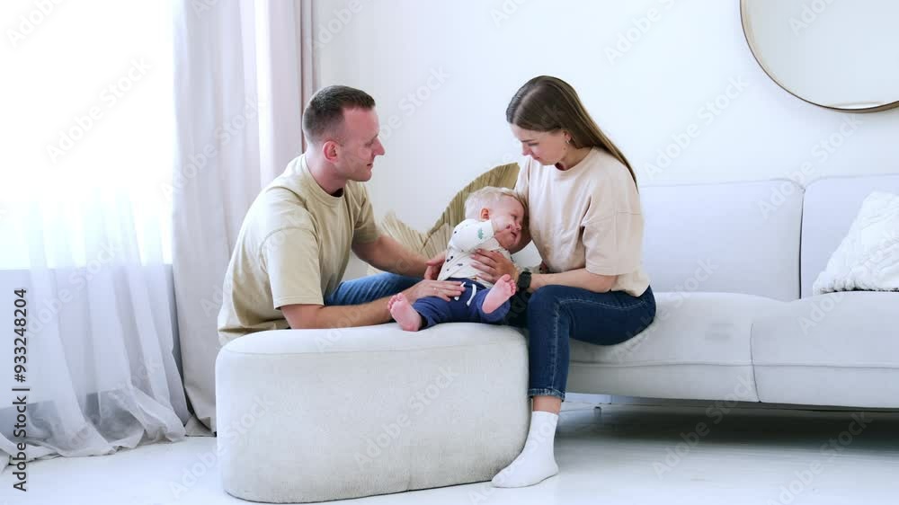 Little baby boy sitting on the sofa is crying bitterly. Mom and dad sitting around him look at their child patiently. Little baby boy sitting on the sofa is crying bitterly. Mom and dad sitting around him look at their child patiently.