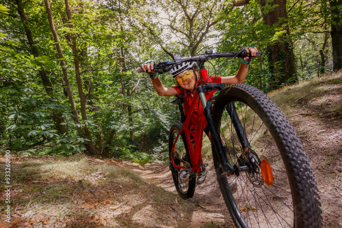 Cyclist kid in red pushing mountain bicycle up a wooded path