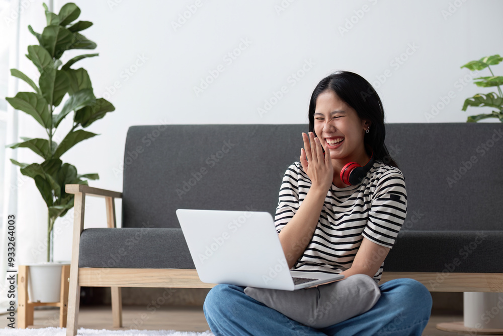 Young Woman Relaxing in Modern Living Room with Laptop and Headphones, Smiling and Enjoying Leisure Time Young Woman Relaxing in Modern Living Room with Laptop and Headphones, Smiling and Enjoying Leisure Time