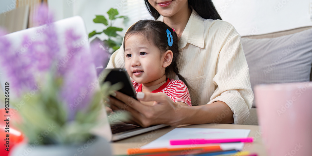 Obraz premium Mother Working from Home with Toddler on Lap Using Laptop and Smartphone in Cozy Living Room