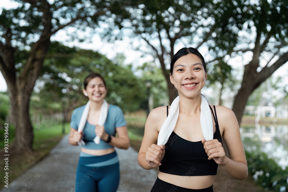 Fototapeta premium Two Women Enjoying a Morning Jog in the Park with Towels Around Their Necks, Smiling and Exercising in Activewear