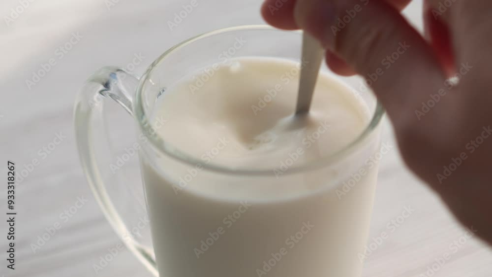 A man without a face stirs white milk in a glass.
Lactose-free milk.
Milk and tea spoon.
teaspoon