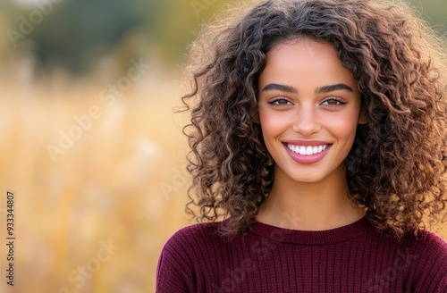 Smiling young woman outdoors with curly hair in a field during golden hour
