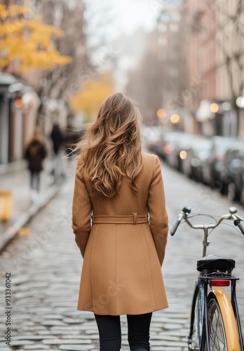 Woman walking in a stylish coat down a cobbled street with a bicycle beside her