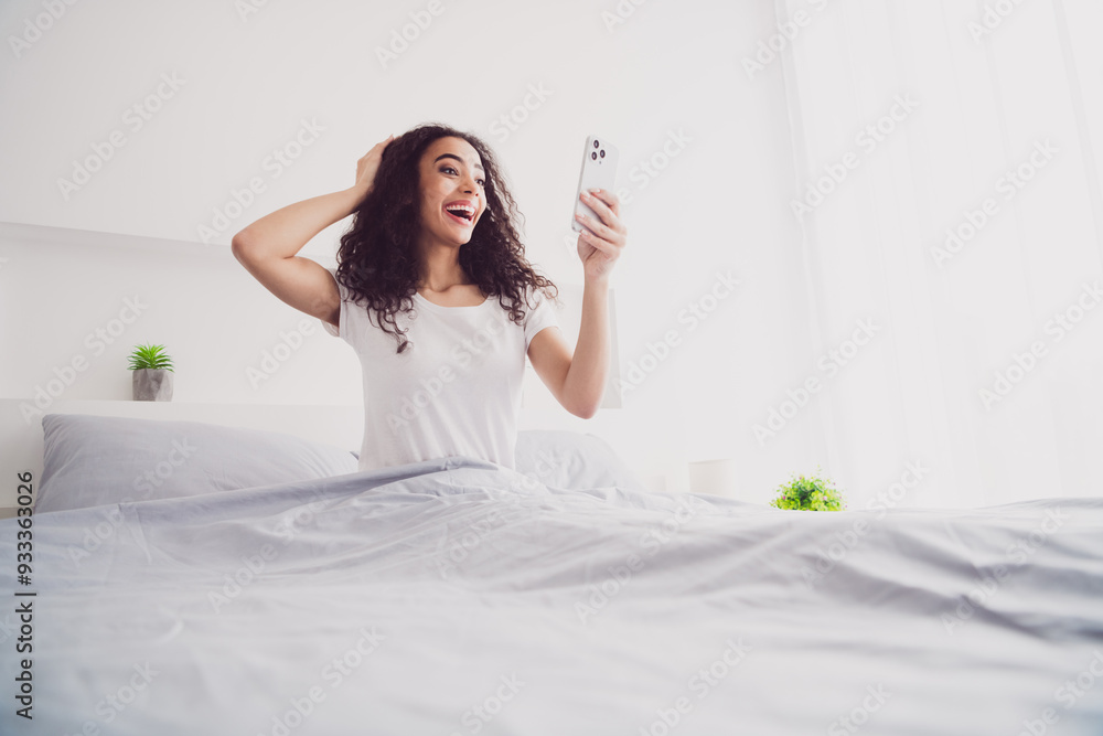 Photo of charming young woman sit bed device shocked good morning vibes awake home bedroom light white interior Photo of charming young woman sit bed device shocked good morning vibes awake home bedroom light white interior