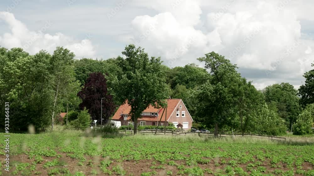 Felder, Bäume und ein Haus im Hintergrund unter bewölktem Himmel Felder, Bäume und ein Haus im Hintergrund unter bewölktem Himmel