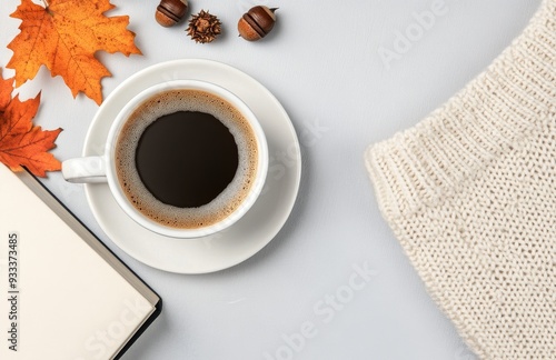 Warm coffee cup with latte art and autumn leaves beside a cozy sweater on a book