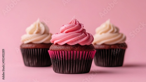 A row of three cupcakes on a pink background with the focus on the pink one in front