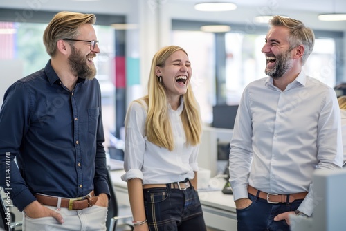 Three business people, two men and one woman, standing in an office, casually dressed blonde woman laughing, modern bright meeting room, corporate team working together.