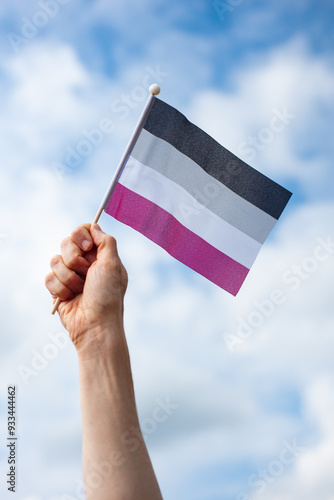 Hand holds up asexual pride flag against sky