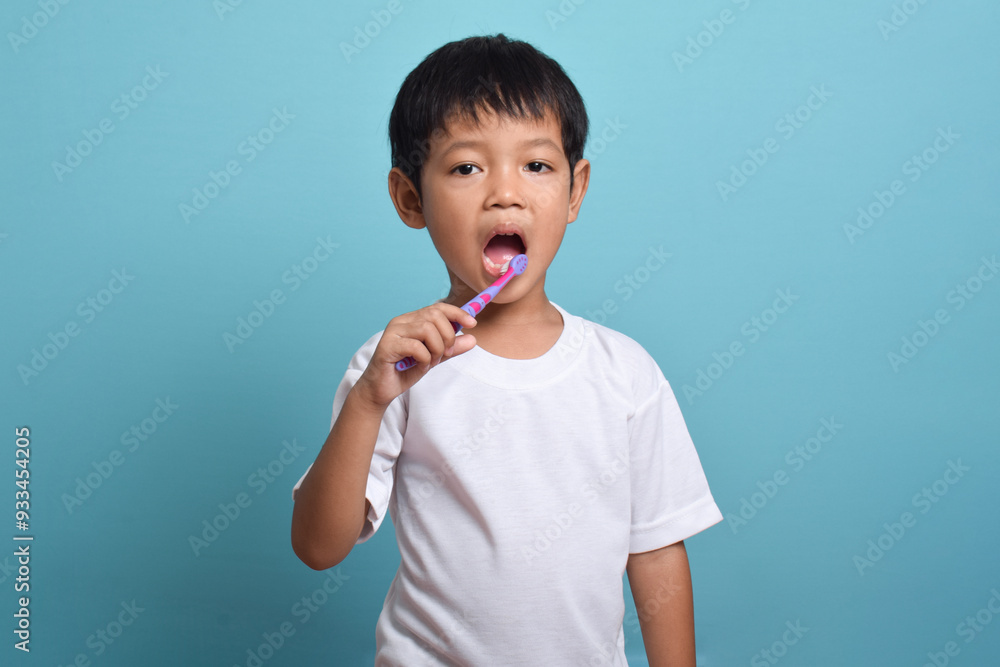 Asian boy with clean teeth brushing his teeth isolated on blue background. Health care, oral hygiene Asian boy with clean teeth brushing his teeth isolated on blue background. Health care, oral hygiene