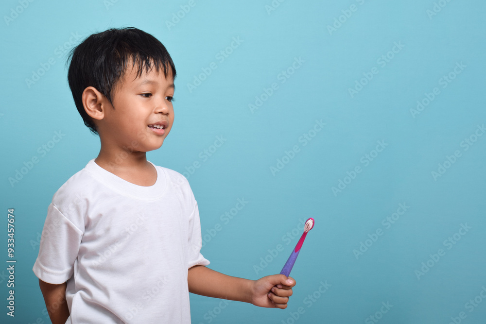 A happy Asian boy holding a toothbrush isolated on blue background. Boy smiles showing his teeth. Children's dental care and hygiene A happy Asian boy holding a toothbrush isolated on blue background. Boy smiles showing his teeth. Children's dental care and hygiene