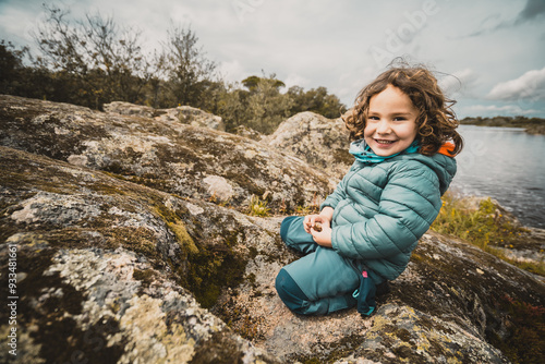 A young girl is sitting on a rock near a body of water