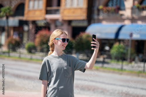 Young girl with long blonde hair takes selfie on city street and smiles