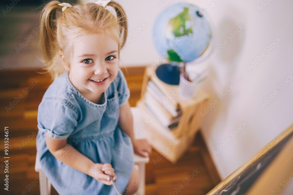 A young girl sits on a chair while drawing next to a globe in a cozy room during the day A young girl sits on a chair while drawing next to a globe in a cozy room during the day