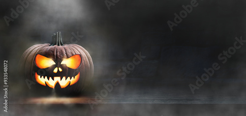 Obraz na płótnie A scary spooky glowing carved halloween pumpkin lantern, Jack O' Lanterns, on the left of a wooden product display bench on a scary halloween night with a dark stone wall background lit from above. w salonie