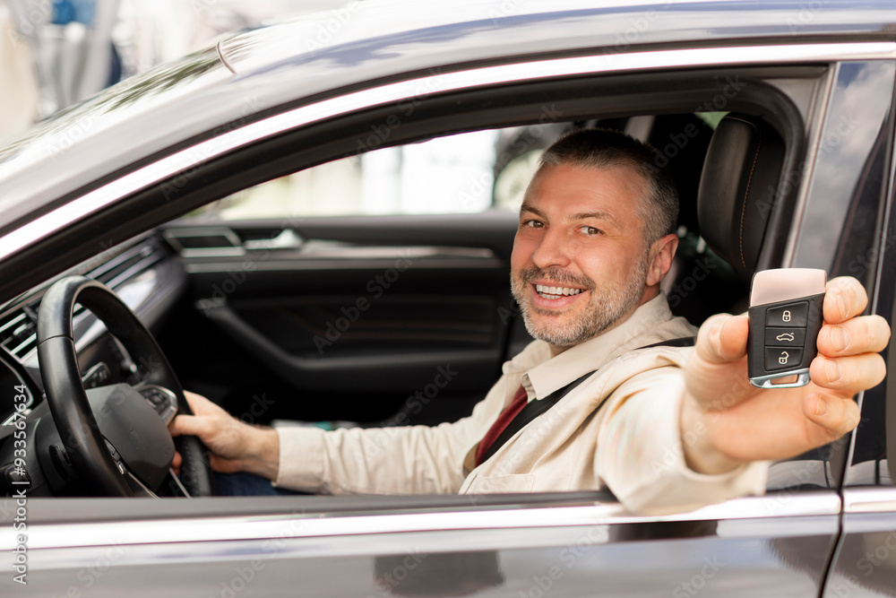 Proud middle aged man car owner showing his new auto key while sitting on driver seat in vehicle, smiling to camera Proud middle aged man car owner showing his new auto key while sitting on driver seat in vehicle, smiling to camera