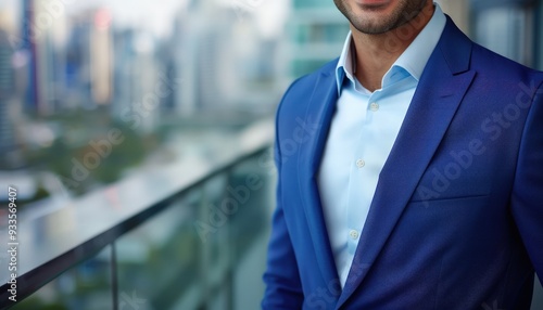 Close-up of a smiling businessman in a blue suit, standing against a blurred modern office and cityscape view, copy space on the right.