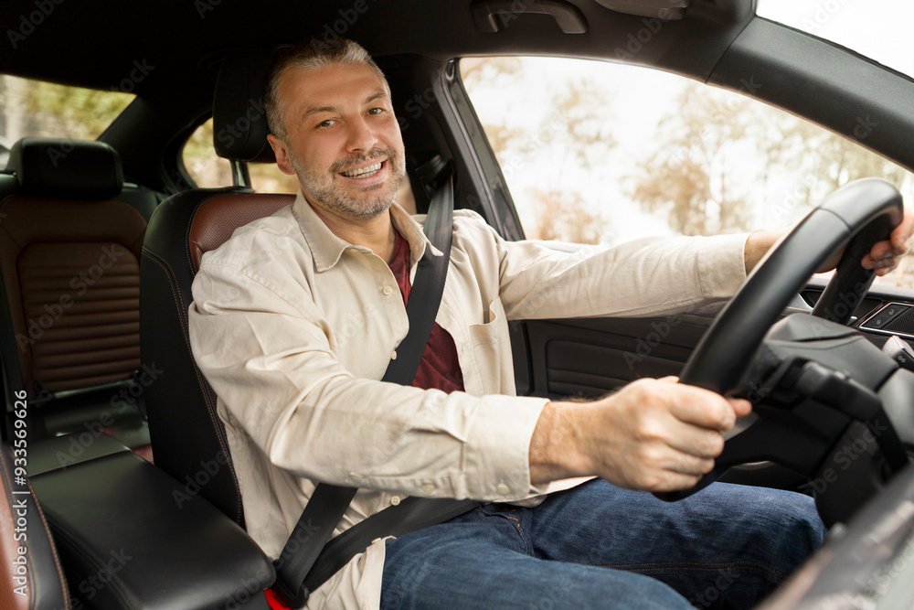 Positive sitting inside his own luxury car, holding hand on steering wheel and smiling at camera. Transportation, automobile renting Positive sitting inside his own luxury car, holding hand on steering wheel and smiling at camera. Transportation, automobile renting