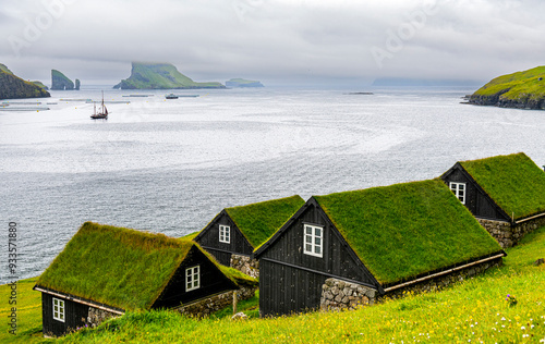 Paisaje de casas feroeses y vistas de Drangarnir ,entre las islas de Vágar y  el islote Tindhólmur en Islas Faroe, un dia de niebla y lluvia fina de Julio