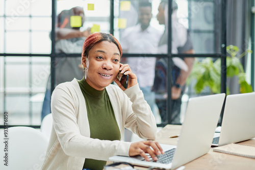 Mobile Communication Concept. Portrait Black Female Talking On Cellphone Working On Pc in Office