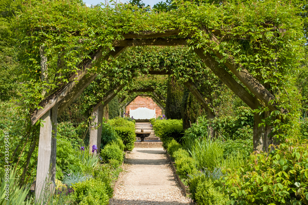 looking down a pathway through a summer garden arbour to a fountain and bench looking down a pathway through a summer garden arbour to a fountain and bench
