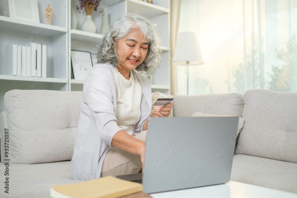Elderly woman with gray hair holding a credit card and using laptop, making payment or shopping online at home. Elderly woman with gray hair holding a credit card and using laptop, making payment or shopping online at home.