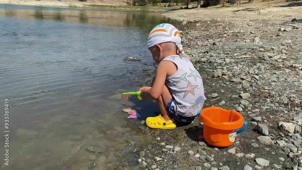 Happy child fisher playing with toy fishing rod catching toy fish in lake in summer Happy child fisher playing with toy fishing rod catching toy fish in lake in summer
