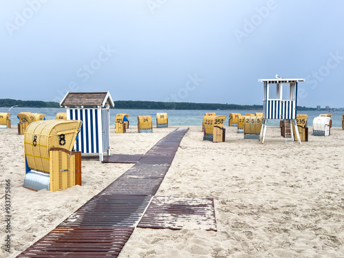 Fototapeta Naklejka Na Ścianę i Meble -  Traditional numbered wicker, reed beach hut, or chair on the sand beach at the coastline of the Baltic Sea in summer Germany with wooden walkway or path