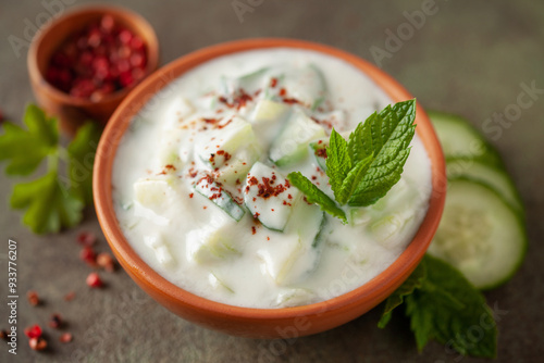 Indian Fresh sauce called Raita with herbs, dahi and sliced cucumber in a bowl on the table. photo