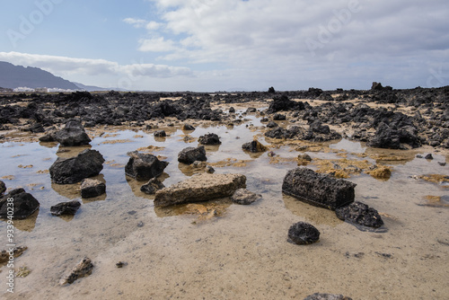 White sand beach with black rocks of volcanic origin. Mountains in the background and sky with big white clouds. Caletón Blanco, Lanzarote, Canary Islands, Spain