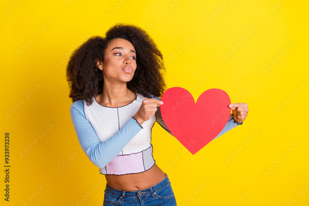 Photo of lovely girl with perming coiffure dressed shirt hold big red heart postcard look empty space isolated on yellow color background Photo of lovely girl with perming coiffure dressed shirt hold big red heart postcard look empty space isolated on yellow color background