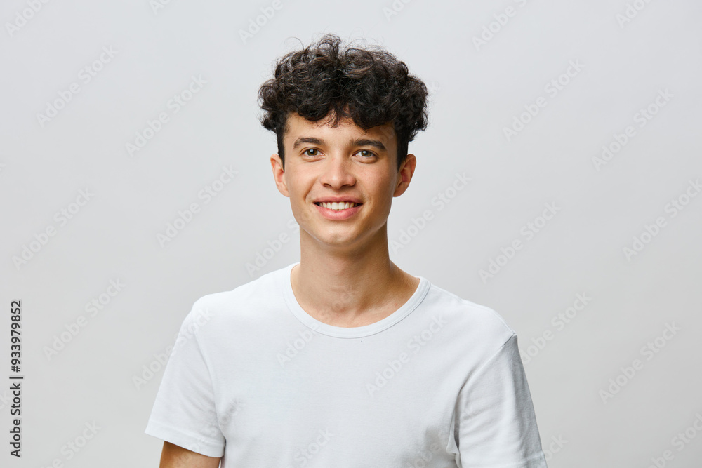 Young man with curly hair smiling in a plain white t shirt against a light gray background, conveying happiness and approachability Ideal for lifestyle and portrait photography Young man with curly hair smiling in a plain white t shirt against a light gray background, conveying happiness and approachability Ideal for lifestyle and portrait photography