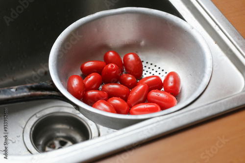 Cherry tomatoes in a metal colander in the kitchen sink. Washing vegetables before eating. Vibrant red color food background. Rustic wooden kitchen metal utensil. Organic food for a helathy snack. photo