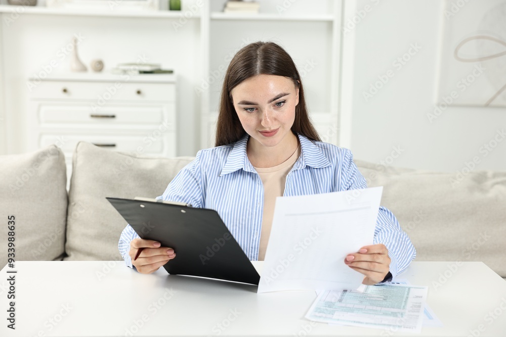 Budget planning. Beautiful young woman with papers at white table indoors Budget planning. Beautiful young woman with papers at white table indoors