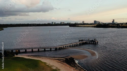 Wallpaper Mural A group of individuals strolls along a wooden pier extending into a calm river as the sun sets behind city buildings. Torontodigital.ca