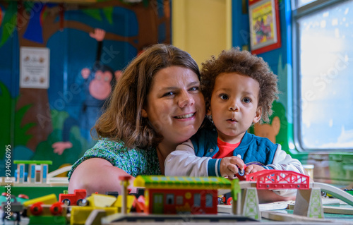 Mom and child play with a train set at nursery, kinder garden. Multi ethnic boy and mother at playtime. mixed race family.