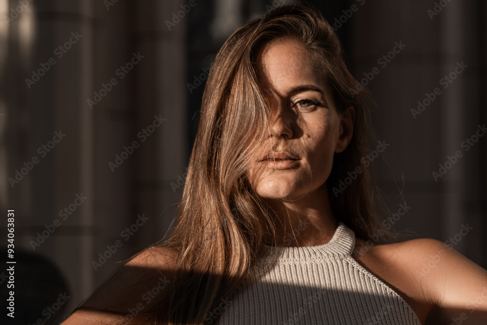 Woman Portrait Sunlit Face Window Light. A woman with long brown hair looks intensely at the camera, her face partially obscured by her hair. The light casts a shadow across her face and body. Woman Portrait Sunlit Face Window Light. A woman with long brown hair looks intensely at the camera, her face partially obscured by her hair. The light casts a shadow across her face and body.