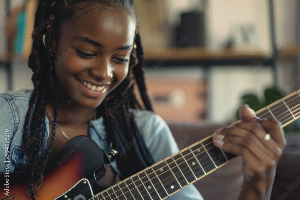 Fototapeta premium Smiling African American teenage girl playing electric guitar in modern living room Leisure activities talent