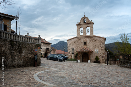 Street of the picturesque village of La Hiruela with the small church of Saint Michael the Archangel with its bell tower on a cloudy day, Madrid, Spain.