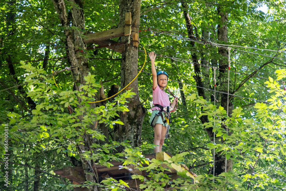 Young girl navigates wooden platforms in forest adventure. She standing and waving her hand. Young girl navigates wooden platforms in forest adventure. She standing and waving her hand.